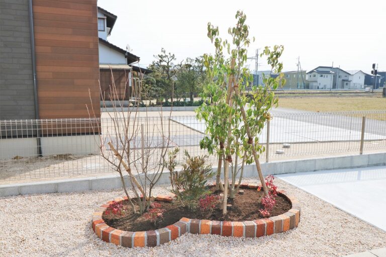 レンガで縁取った花壇に若木と低木を植えた玄関まわりの施工例