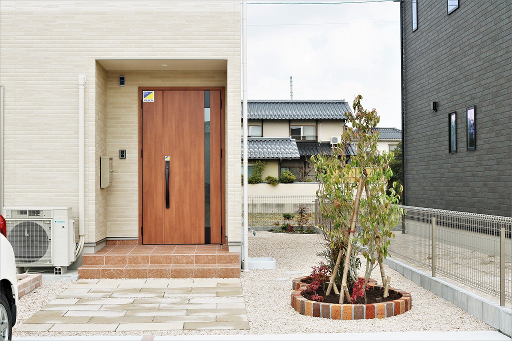 支柱で固定した若木と低木を植えた玄関先の施工例