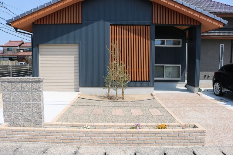 門柱とオリーブの木、玉砂利を組み合わせた住宅の玄関まわり