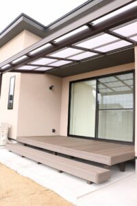 ポリカーボネート屋根付きの広いウッドデッキと掃き出し窓、ベンチ状の造作