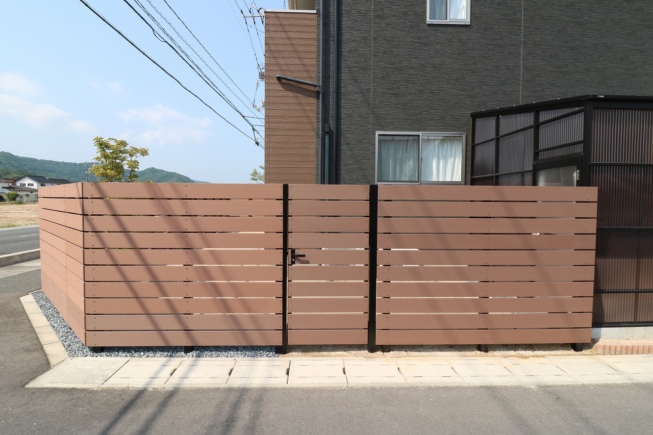 木目調の横板張り目隠しフェンスと開き戸のある住宅の外構