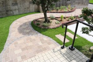 曲線を描く石畳のアプローチと円形の植栽帯がある庭