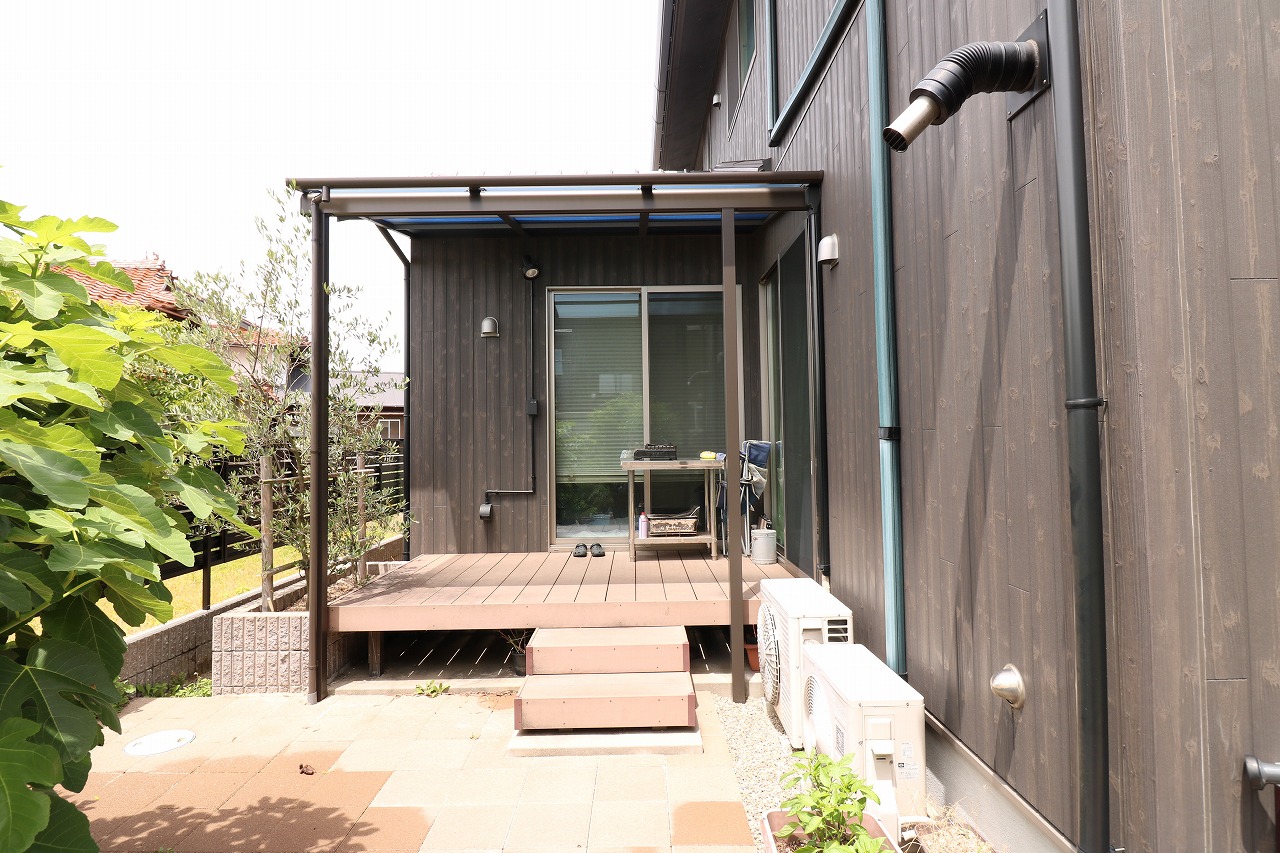 木目調の外壁とパーゴラ風の屋根に一体化したウッドデッキ、オリーブの木と階段