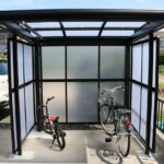 ポリカーボネート製の側面パネルを備えたカーポートに自転車と車が置かれている様子