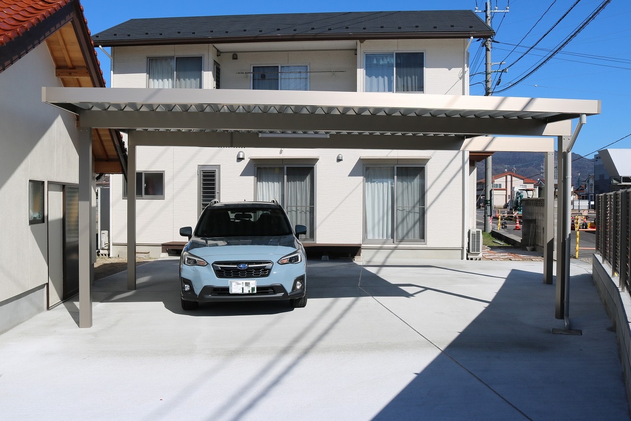 住宅前に設けられた開放的なフラット屋根のカーポートと駐車された車