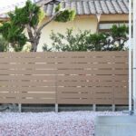 板と板の間に隙間をとったベージュの横板目隠しフェンスと、背後に見える既存の庭木