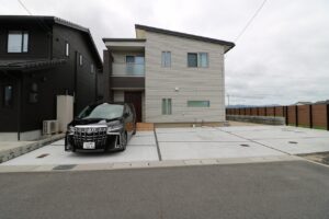 白い土間コンクリートの駐車スペースと玉砂利の植栽帯を組み合わせた施工例