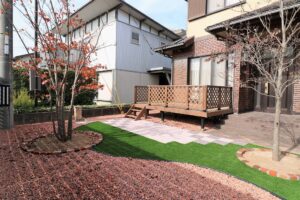 格子状の手すりを設けたウッドデッキと、人工芝・敷石・紅葉した庭木を組み合わせた庭の施工例