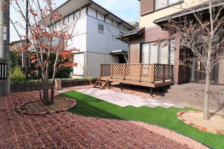 格子状の手すりを設けたウッドデッキと、人工芝・敷石・紅葉した庭木を組み合わせた庭の施工例