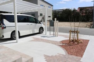 白いカーポートの脇にシンボルツリーと化粧砂利で整えたアプローチのある住まい