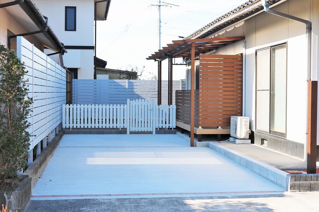 木調フェンスと白いフェンスで囲まれた庭に設けた木製パーゴラ付きウッドデッキ