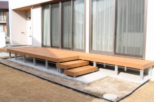 リビングの掃き出し窓に沿って広がるL字型の人工木ウッドデッキと階段
