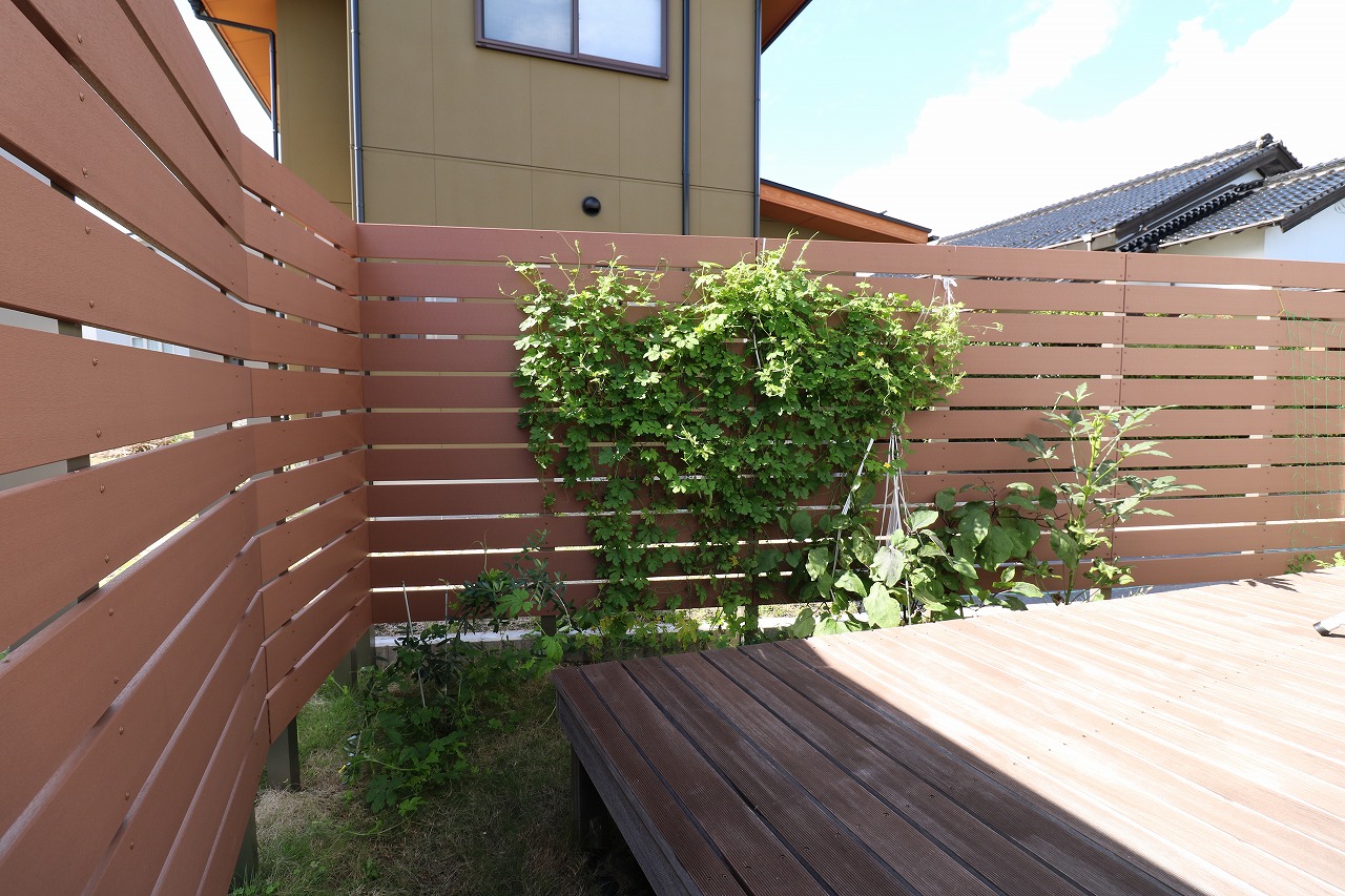木調の目隠しフェンスにつる性植物を這わせたウッドデッキのくつろぎ空間