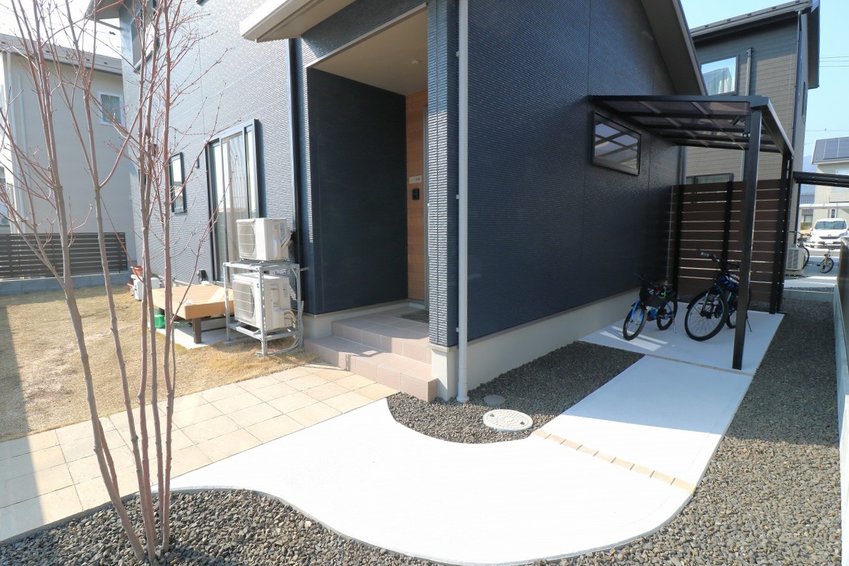 自転車を置いた小屋根付きスペースと木調の目隠しフェンスがある玄関まわりの施工例