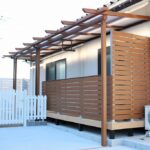 出雲の庭に、外とつながるウッドデッキという居場所 木製パーゴラと木調フェンスに囲まれた白い扉のあるウッドデッキスペース