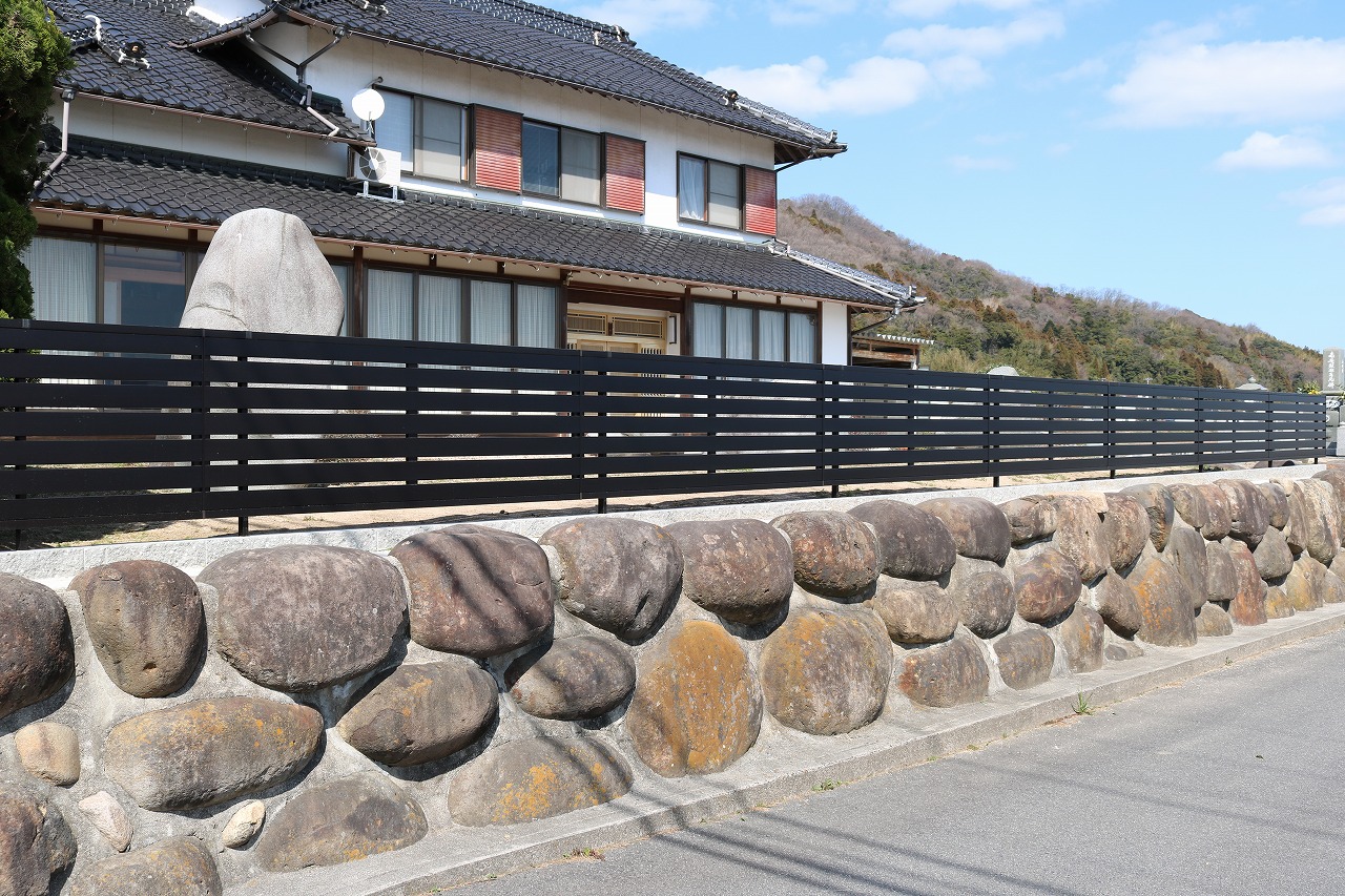 玉石積みの塀の上にすき間をとった黒い横板フェンスを設けた施工例