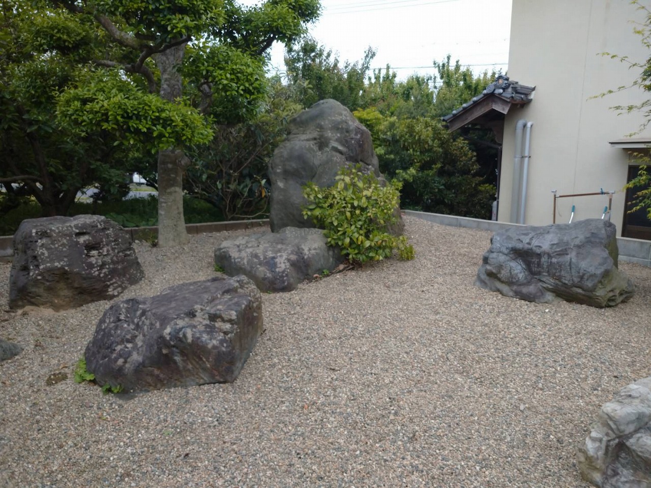 化粧砂利を敷いた地面に大小の景石を据え、低木と庭木を組み合わせた和の庭の施工例