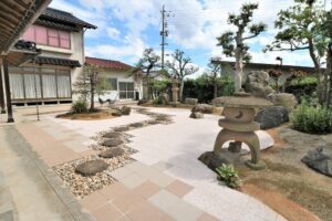 縁側と窓に面した和風の庭。飛石と敷石の通路、石灯籠、松や庭木を配した施工例