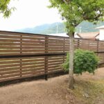 庭木の緑に囲まれた木調の横板目隠しフェンスの施工例