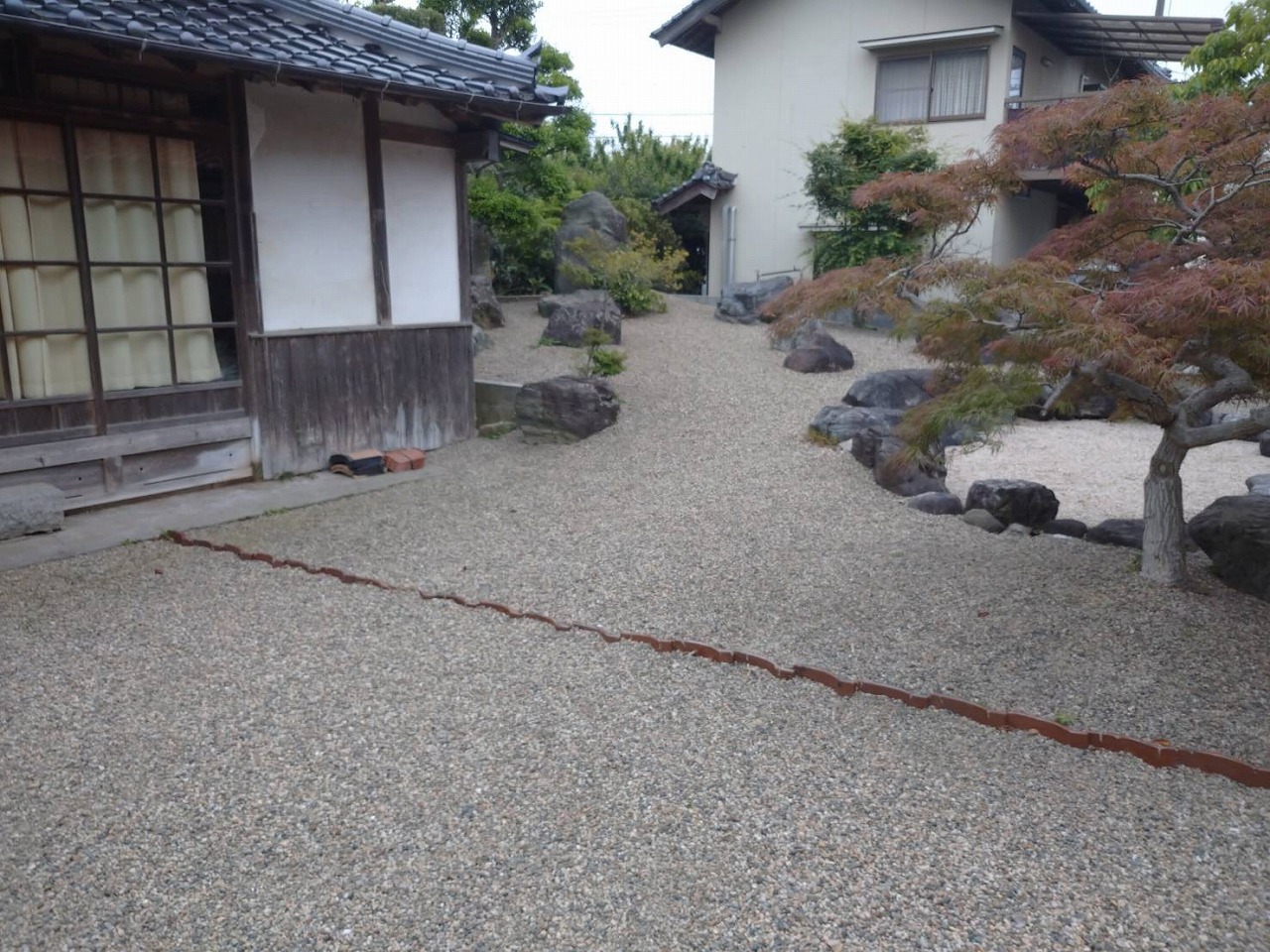 石を配した砂利敷きの庭と年月を経た紅葉した木