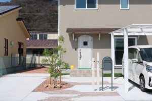 玄関のすぐ横に設けた白いカーポートと、植栽やポストを配したアプローチの施工例