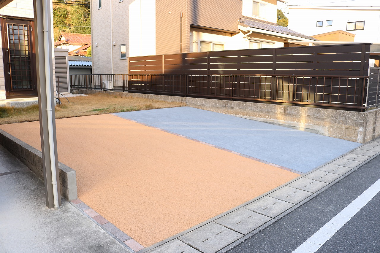 ダークカラーのアルミルーバーフェンスを設置した駐車スペースと隣接する庭