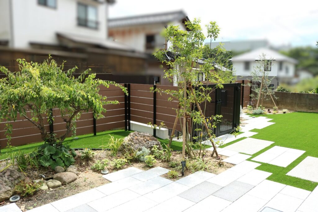 リノベーション後の庭。木目調フェンス、人工芝、石張りのアプローチと植栽