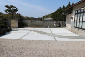 松の木と石積みのある和風の住まいの前に、石張りの曲線が通る土間コンクリートの駐車スペースを設けた施工例
