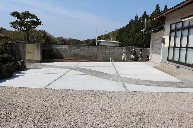 松の木と石積みのある和風の住まいの前に、石張りの曲線が通る土間コンクリートの駐車スペースを設けた施工例